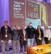 Image of training staff on stage behind bannerreading "you're safe here"