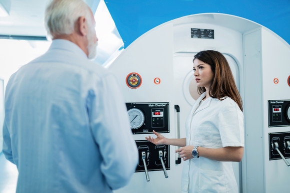 Young doctor and senior man stood in front of hyperbaric oxygen chamber