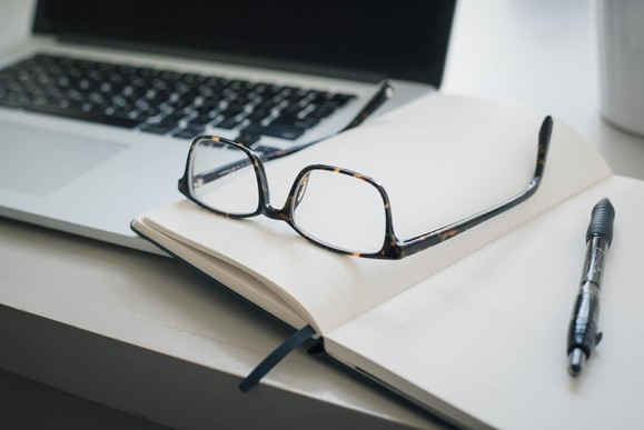 Desk with laptop, glasses, open notebook and pen