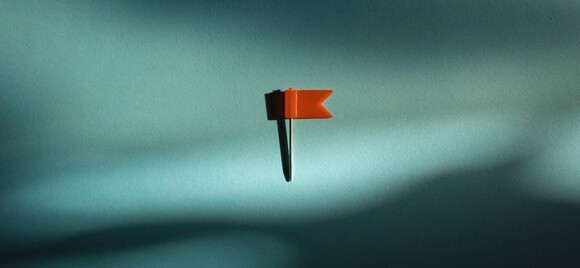 Photograph of a pin with red tag against a plain blue background