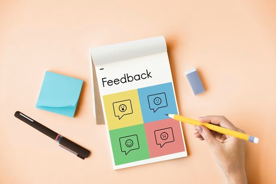 A notepad with the word feedback written upon it, and four different coloured boxes, each with speech marks depicting a different facial expression.