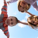 Three children look down over the photographer with bright blue sky in the background