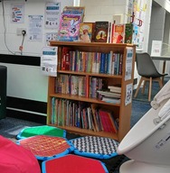 Book shelves with lots of childrens books surrounded by seating including mats and bean bag. 