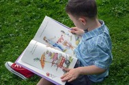 Child sat on grass reading a book