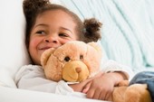 child smiling whilst hugging her teddy bear