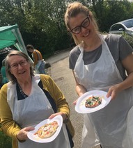 Two women showing pizzas they've made to the camera