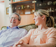older gentleman laughing along with younger lady both sitting on sofa
