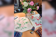 Decorative flowers surrounded by paintings flowers and paints on a table