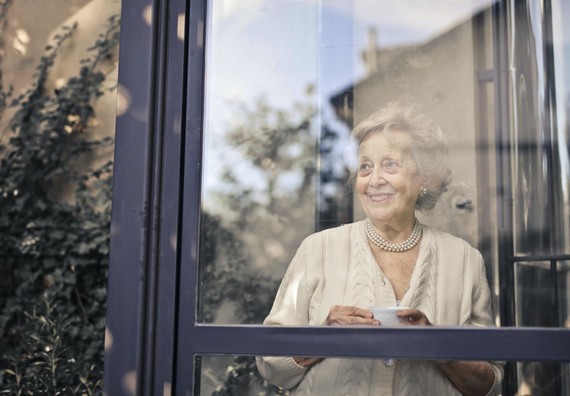 Elderly lady stood in from of a window smiling