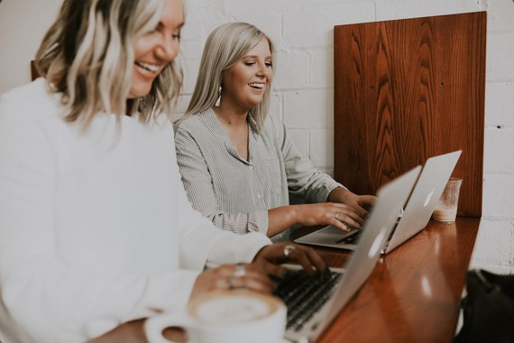 two smiling female school_office staff working on laptops 