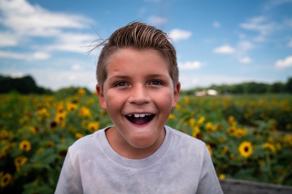 boy standing in a field of sunflowers smiling
