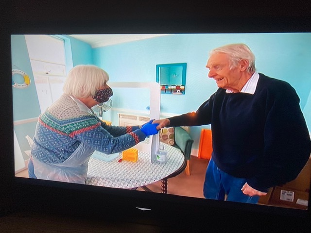 A femal visitor to a care home shakes a hand with a male resident.