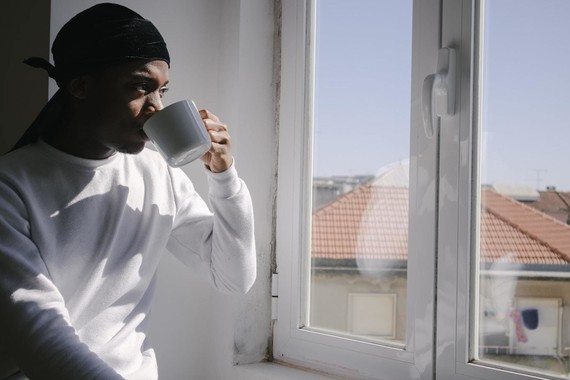 young man looking out of window with a mug in hand