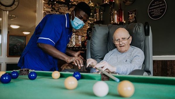 A care assistant helps an eldery man play snooker