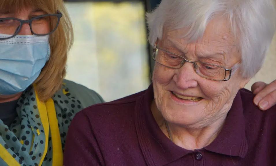 Social care worker looking over shoulder of older woman in care setting