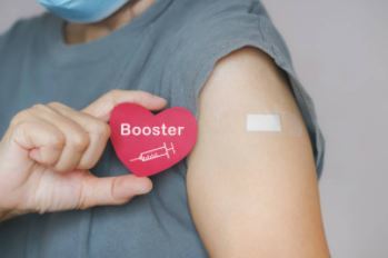 A woman holds a symbol: red hart with a syringe and the word 'booster'