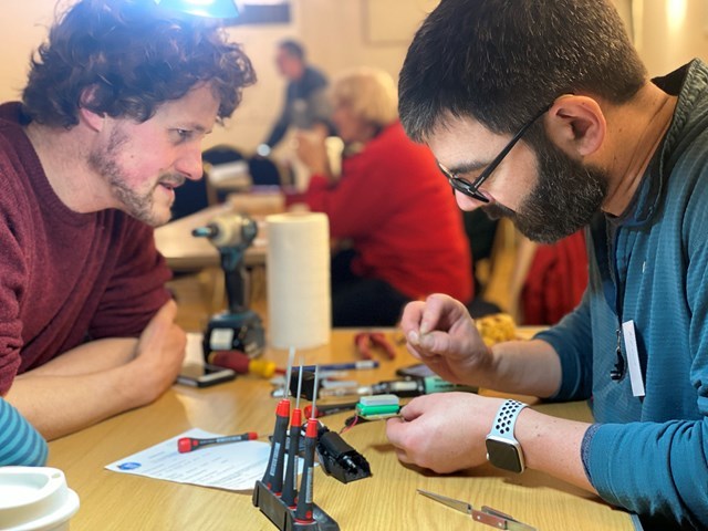 Repair Cafe - two people at a table, and one of them is trying to fix the object in front of him