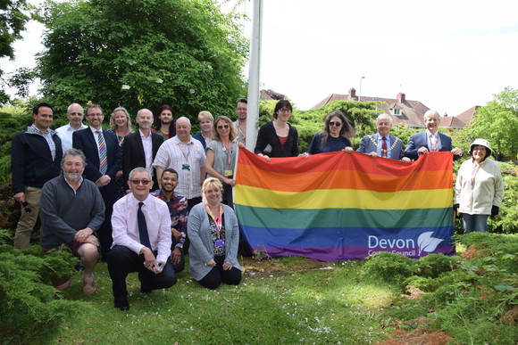 A group, which includes the Chairman of Devon County Council and the Chief Executive, posing with the Pride flag at County Hall