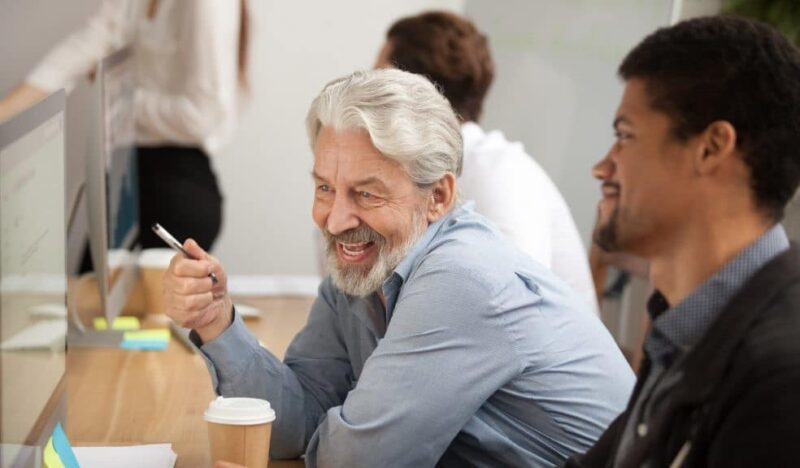 Grey haired man smiling facing computer screen