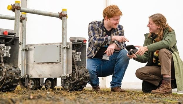 Male and female farmers crouching looking at earth and talking