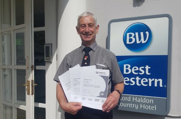 Simon Adams, an employee at the hotel, attending the training course. He is stood at the front of the hotel with his training certificate