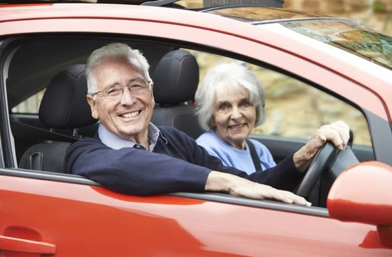 Older man and woman driving a red car