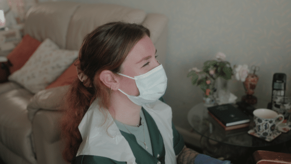 A young care worker, smiling, and wearing a mask