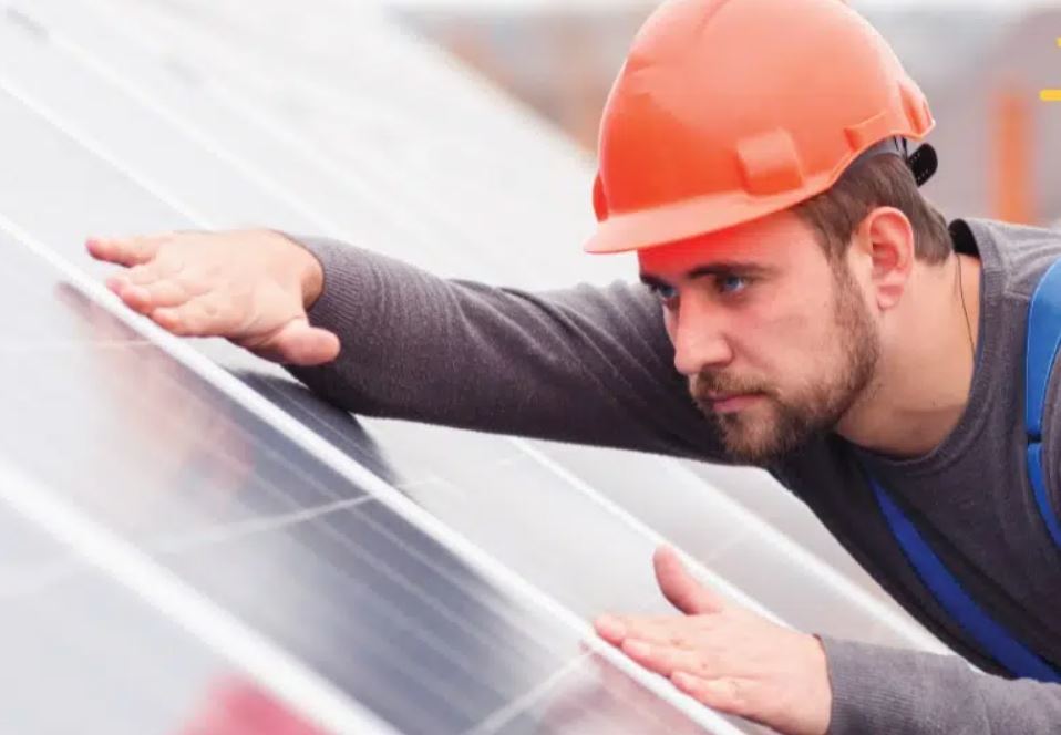 Roofer with orange hat hard on a roof holding down a solar panel