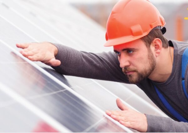 Man on a roof wearing a hard hat, fitting a solar panel to the roof.