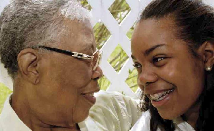 Carers older black female with short grey hair and glasses looking caringly into black female teenager eyes
