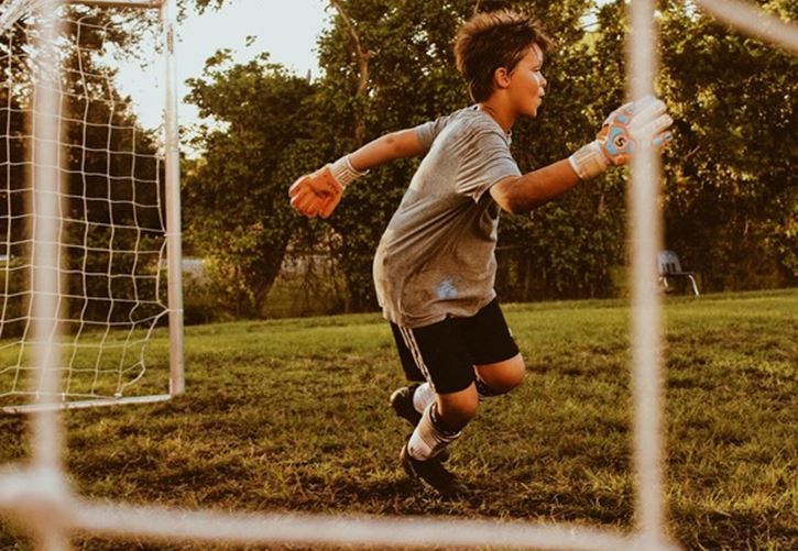 Boy with football gloves jumping to save the ball in goal