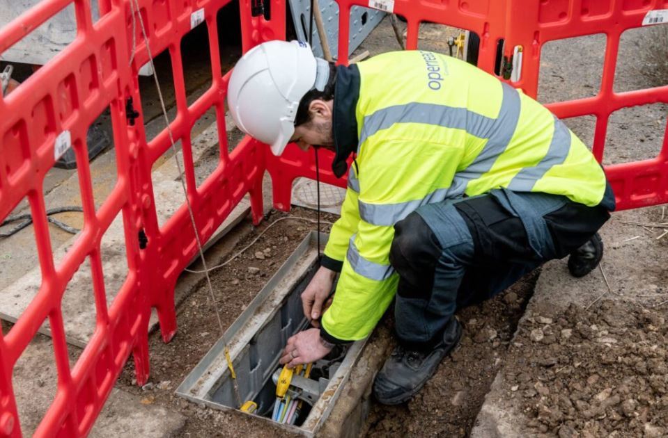 Openreach worker kneeling down and using tools to lay broadband fibre cables through a hole in the ground