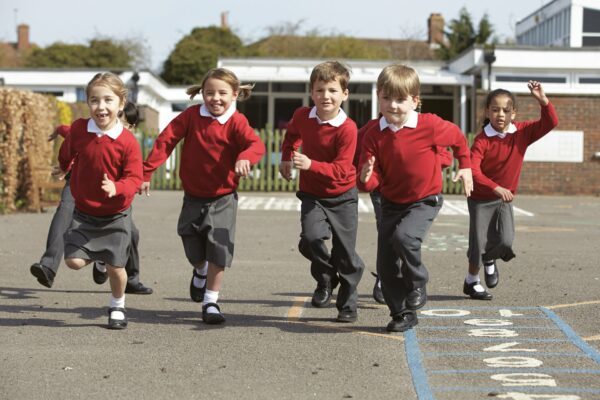 A line of young school children, in school uniform, running towards the camera across the playground