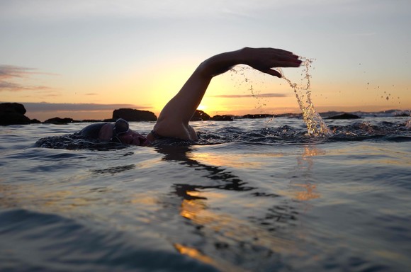 Two people swimming, front crawl, in the sea at sunset