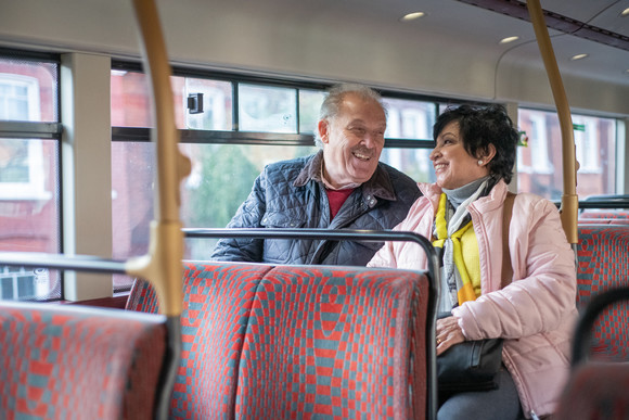 An older couple sitting on the top deck of a bus, laughing with each other