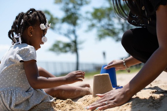 A young black girl laughing as she builds a sandcastle with her mum