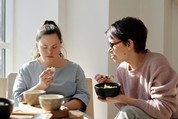 Down syndrome woman eating and sitting by a white wall