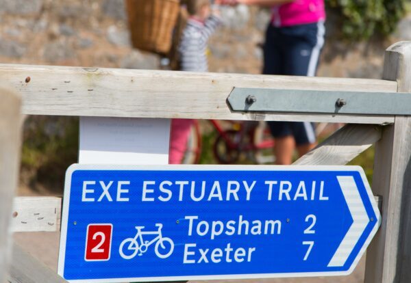A blue sign fixed to a gate on the Exe Estuary Trail, describing the distance to Topsham and Exeter 