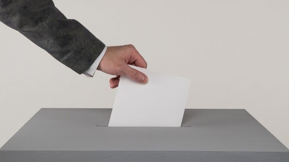 A hand posting a ballot slip into a ballot box