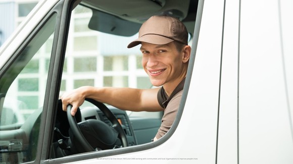 A driver of a van looking out of his side window at the camera smiling