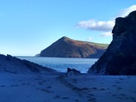 A sandy beach in shadow with the sea in the distance and a headland in bright sunlight beyond it