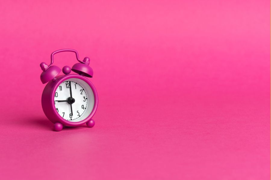 A pink alarm clock, against a pink background