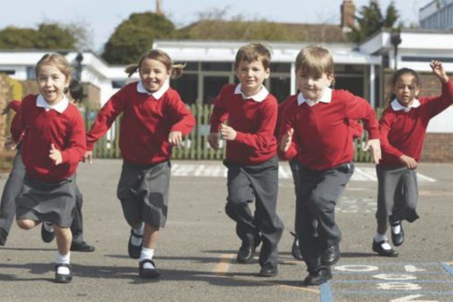 A line of Primary School children running across a playground, playing.
