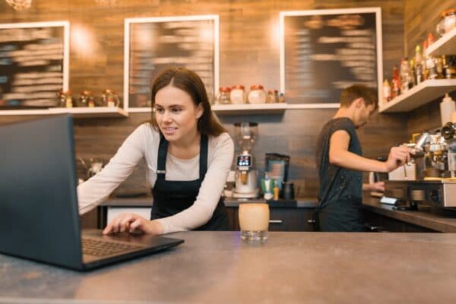A coffee shop worker behind the counter using her laptop