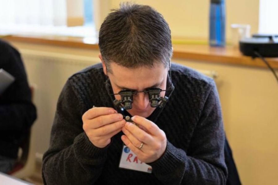 A man with a magnifying glass examining a very small item, to repair it