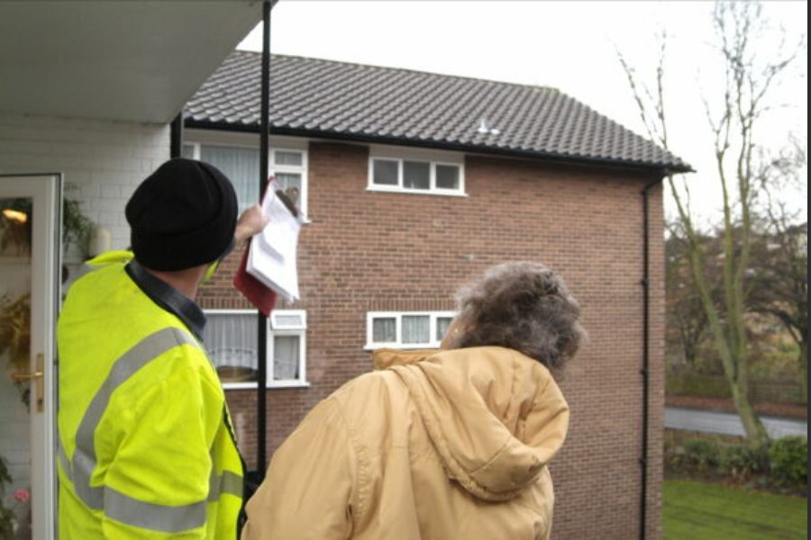 A trading standards officer talking to a home owner and both looking up at the home owner's roof