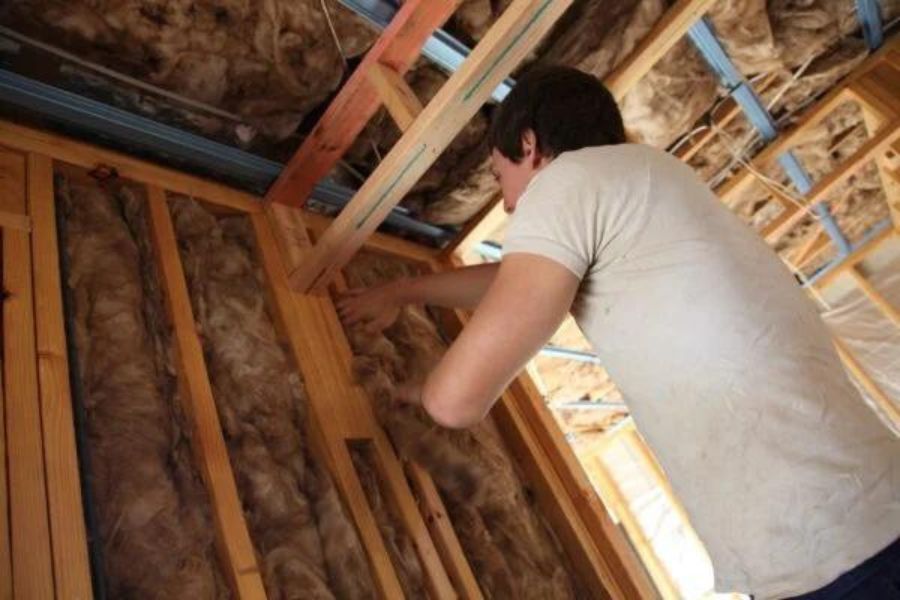 A person fitting wall insulation into a stud wall