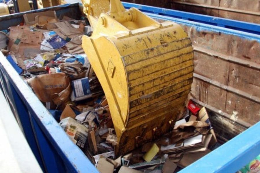 A digger with its bucket in a waste skip