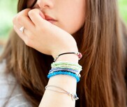 Close up of a white girl's arm, with lots of friendship bracelets around it. Her hand is covering her mouth