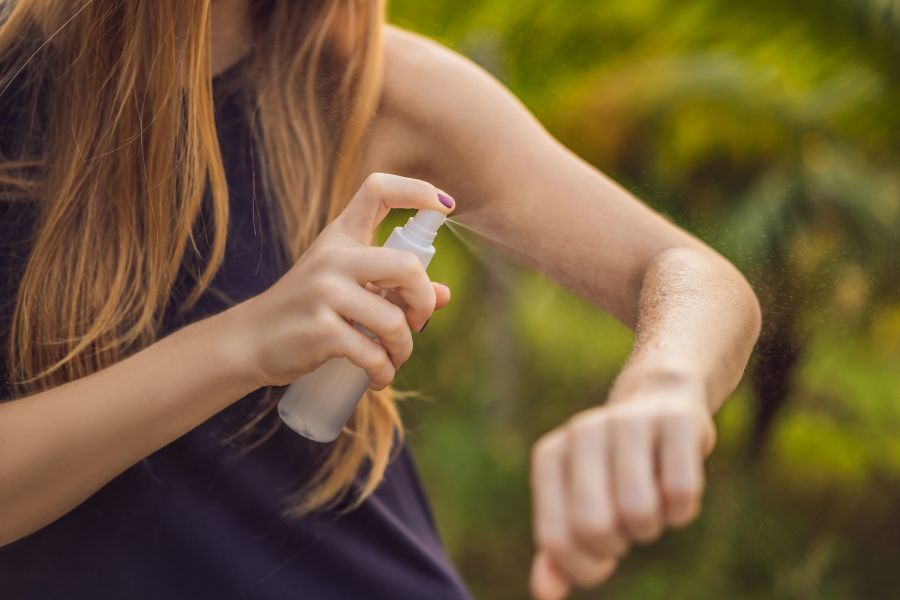 A young person spraying her arm with insect repellent